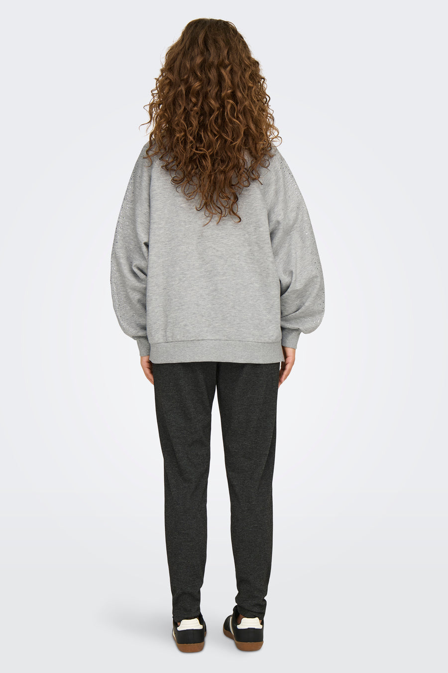 Grijze sweater van ONLY®, lange ballonmouwen versierd met strass, gedragen met een geruite broek en zwarte sneakers.