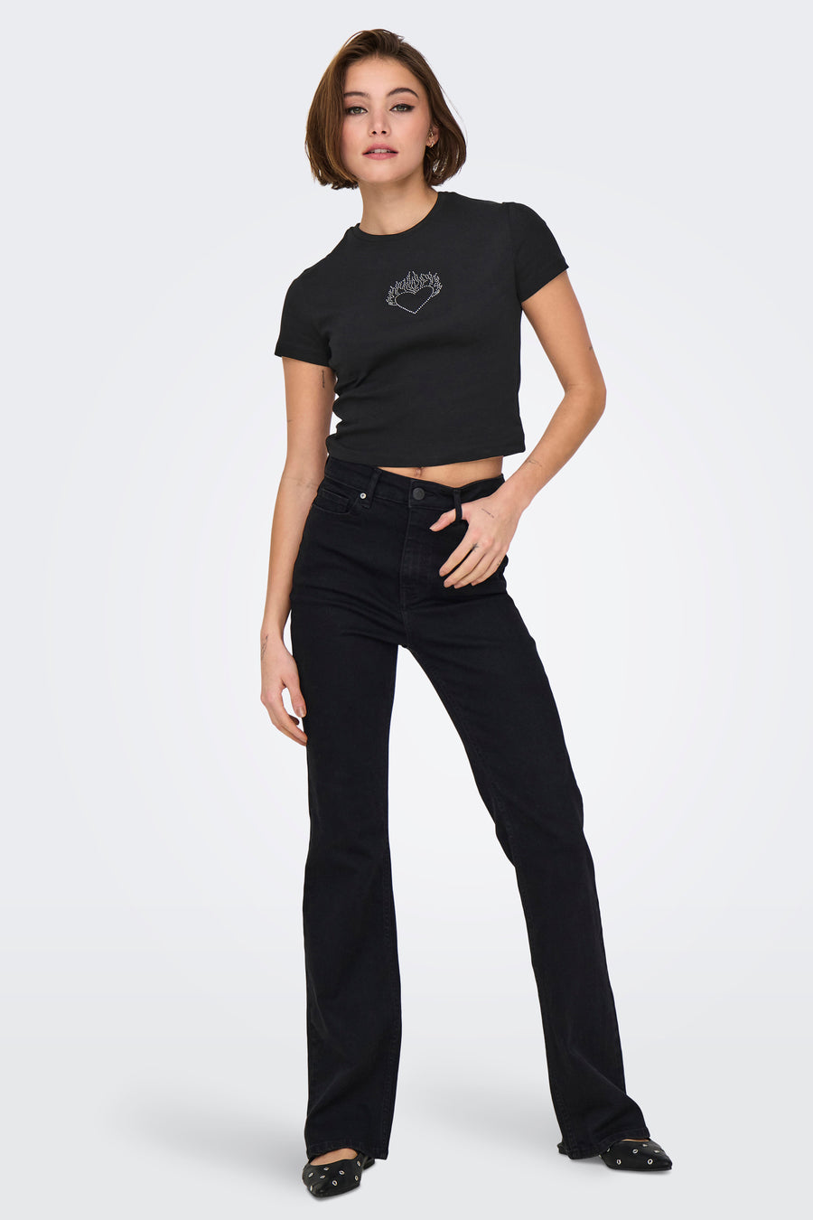 T-shirt noir à manches courtes par ONLY®, orné d'un motif cœur scintillant, porté avec un jean noir et des chaussures plates.