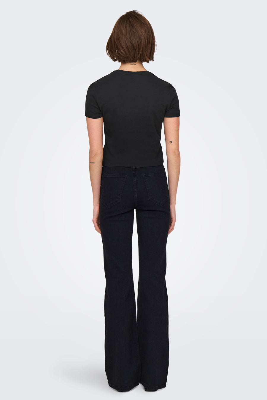 T-shirt noir à manches courtes de ONLY®, porté avec un jean évasé noir uni, vue de dos.
