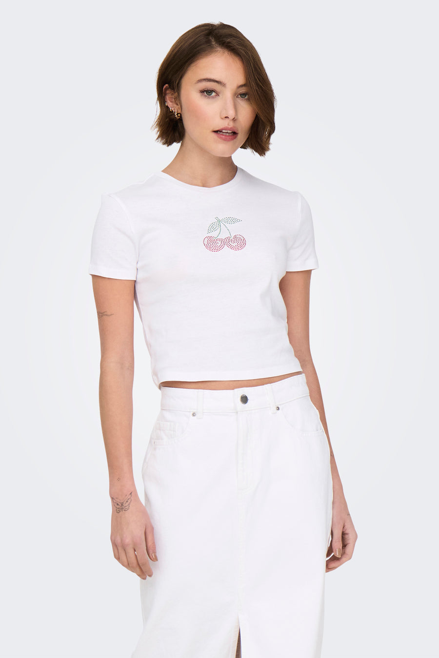 T-shirt blanc à manches courtes de ONLY, orné de cerises décoratives, porté avec un pantalon blanc.
