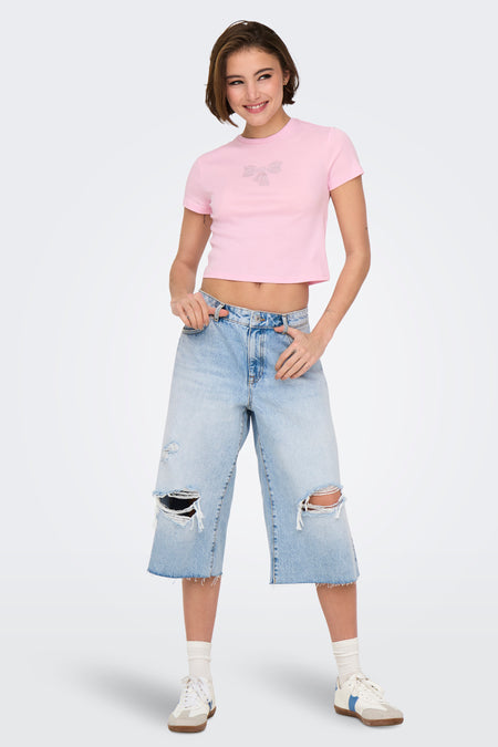 T-shirt rose à manches courtes de ONLY, orné d'un nœud, porté avec un pantalon large déchiré et des baskets.
