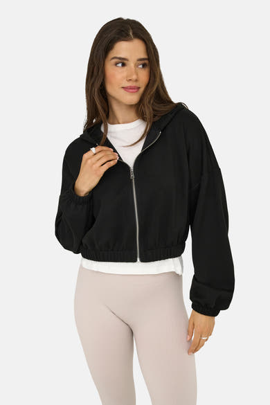 Zwarte bodywarmer van ONLY, met ritssluiting, gedragen over een wit T-shirt en beige geribbelde leggings.
