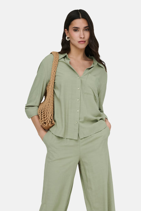 Chemise verte de JDY à manches longues, texture légère, portée avec un pantalon assorti et un sac filet marron.