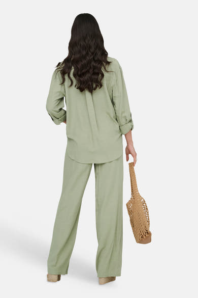 Chemise longue verte de JDY à la coupe décontractée, manches retroussées, portée avec un pantalon assorti et un sac en filet.