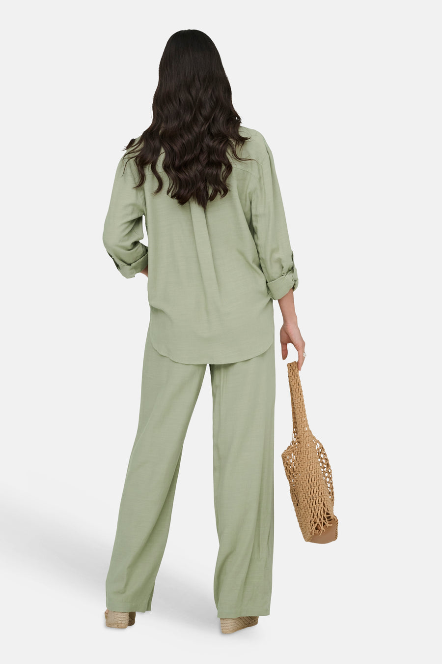 Chemise longue verte de JDY à la coupe décontractée, manches retroussées, portée avec un pantalon assorti et un sac en filet.