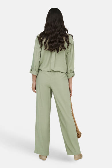 Pantalon vert de JDY, coupe ample et jambes larges, porté avec un haut assorti et un sac en filet.

