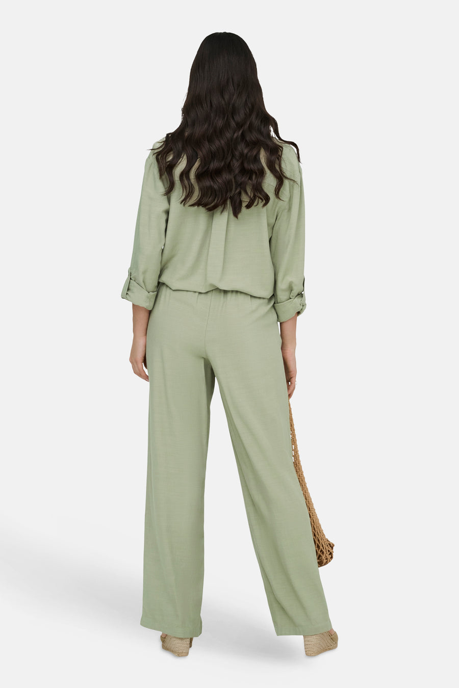 Pantalon vert de JDY, coupe ample et jambes larges, porté avec un haut assorti et un sac en filet.
