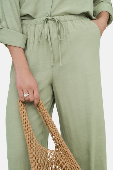 Pantalon vert en tissu, par JDY, avec cordon de serrage à la taille et sac beige en macramé.
