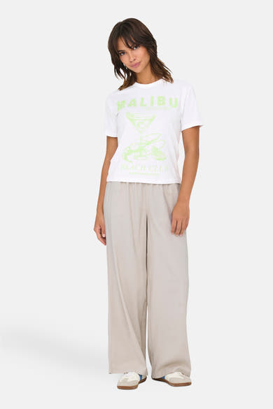 Wit T-shirt met korte mouwen van ONLY®, met Malibu Beach Club-print, gedragen met een beige wijde broek.