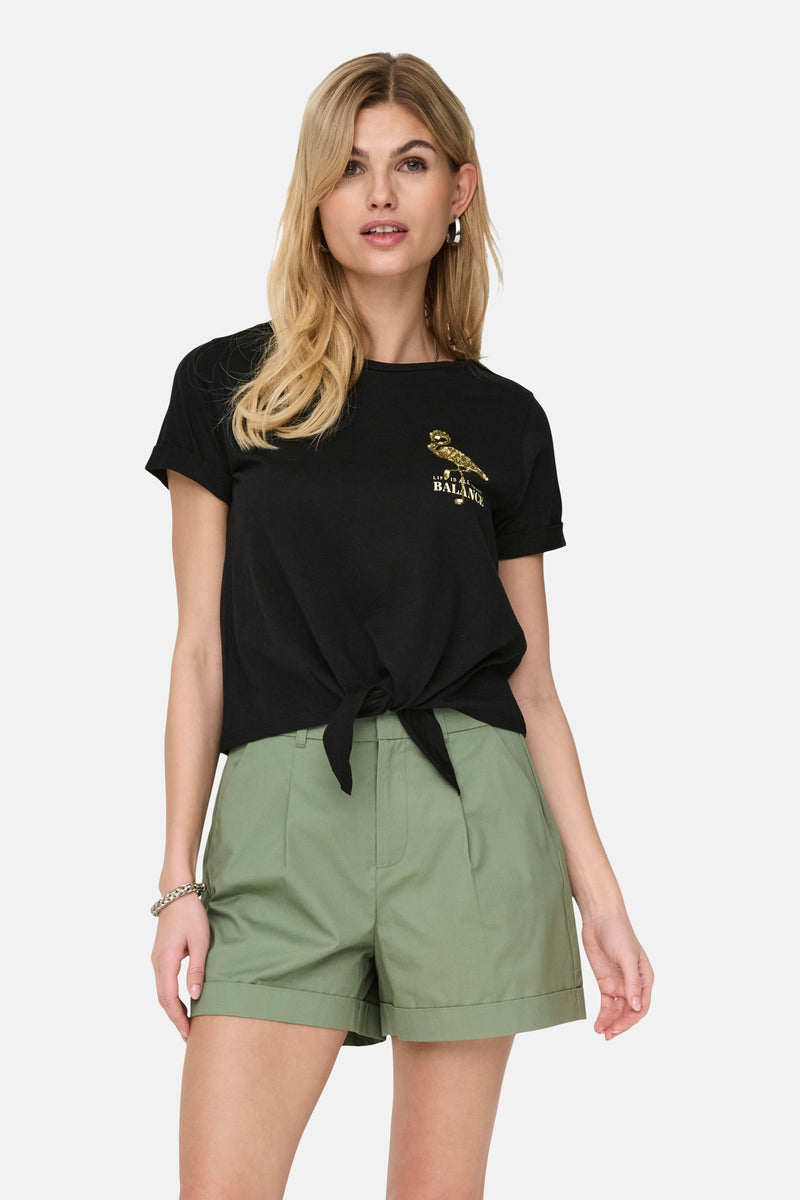 Zwarte t-shirt met korte mouwen van ONLY, versierd met een gouden vogelmotief en gebonden op de voorzijde, gedragen met een groene broek.