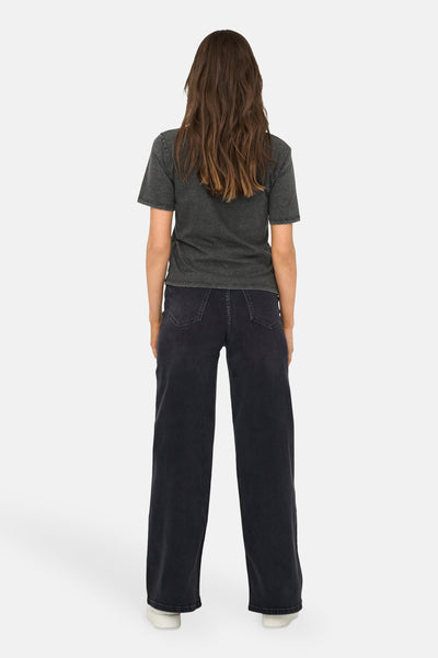 Zwart T-shirt met korte mouwen van ONLY, gedragen met een donkere wijde broek en witte sneakers.
