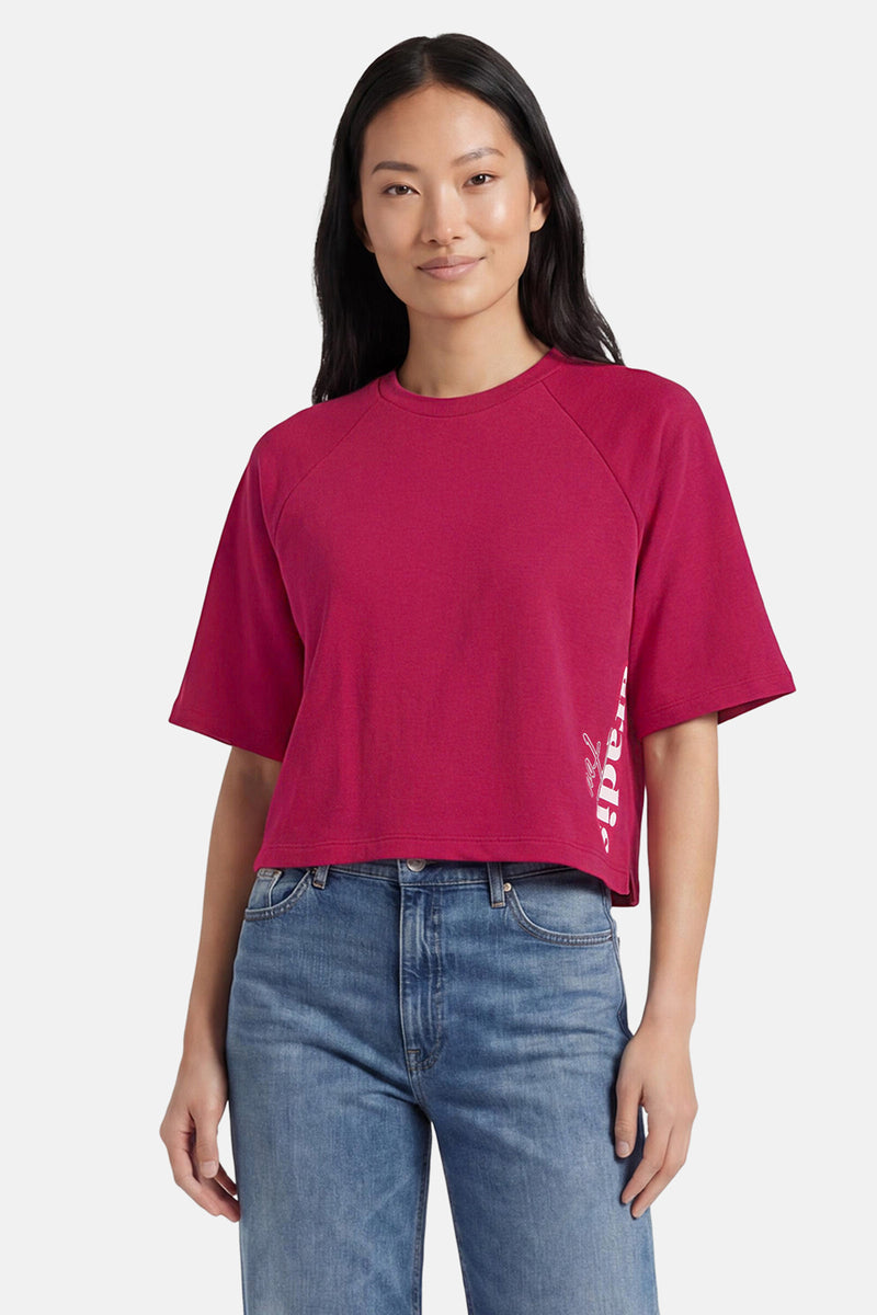 T-shirt rose de ONLY® à col rond, manches courtes raglan, coupe courte et inscription verticale blanche sur le côté, porté avec un jean bleu.