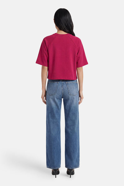 T-shirt uni rose à manches courtes de ONLY®, coupe ample et courte, porté de dos avec un jean bleu et des talons noirs.