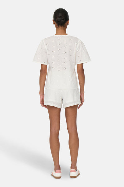 Chemisier blanc à manches courtes de JDY avec broderie anglaise, porté avec un short blanc et des baskets roses.