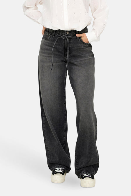 Jean droit en denim noir par ONLY, avec cordon de serrage, porté avec une chemise blanche.
