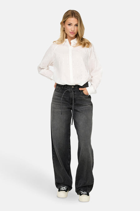 Jean droit en denim noir par ONLY, porté avec une chemise blanche à paillettes et des baskets compensées noires et blanches.
