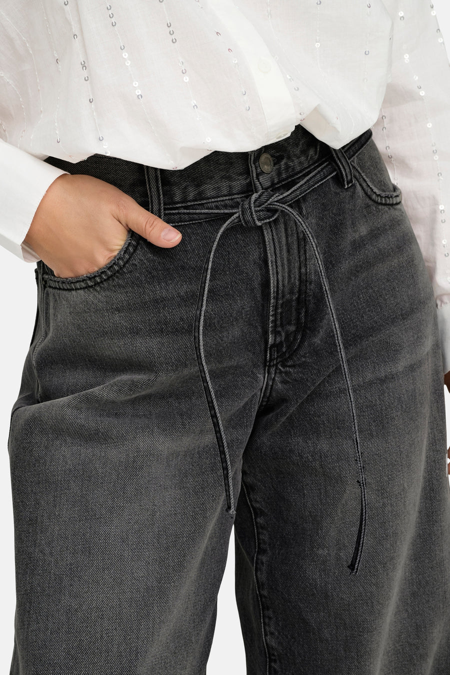 Jean droit en denim noir de ONLY, avec une ceinture nouée et porté avec une chemise blanche à sequins.

