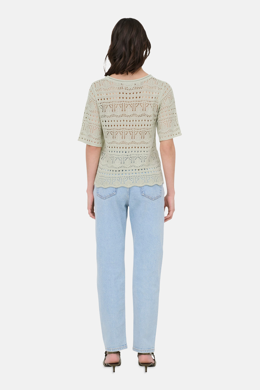 Pull à col rond vert de JDY, avec motif ajouré, porté avec un jean bleu clair et des chaussures à talons noirs.