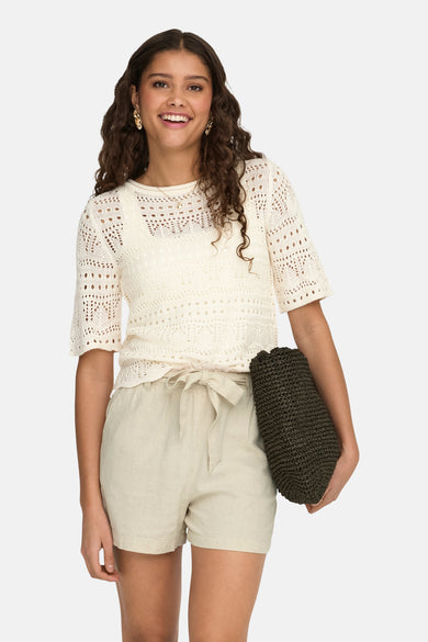 Ecru ronde hals trui van JDY, ajour met korte mouwen, gedragen met een high-waist linnen short en gouden oorbellen.