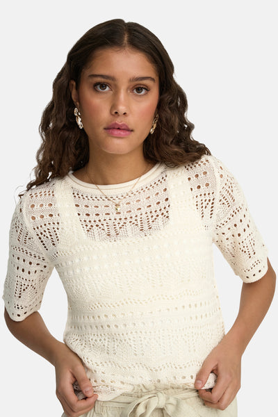 Ecru ronde hals trui van JDY met ajourpatroon, gedragen met een beige hoge taille broek, gouden oorbellen en een fijne ketting.