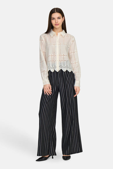 Chemisier blanc en dentelle de JDY, avec un motif ajouré et porté avec un pantalon à rayures verticales.