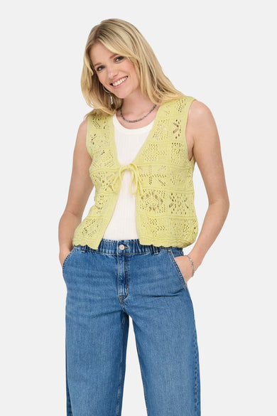 Gele gebreide bodywarmer van ONLY, gedragen over een witte tanktop en een high-waisted jeans.