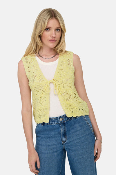 Gilet jaune en maille by ONLY, avec un motif ajouré et porté sur un t-shirt blanc et un jean.
