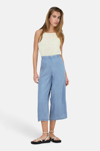 Beige hemd zonder mouwen, van ONLY®, gedragen met een lichtblauwe wijde broek en zwarte sandalen met bandjes.