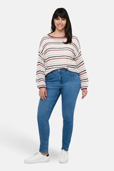 Pull à col rond multicolore de CARMAKOMA, rayures horizontales, porté avec un jean bleu et des baskets blanches.
