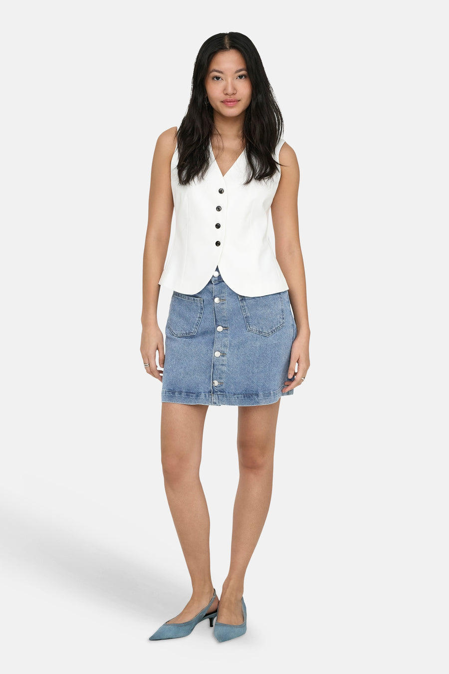 Jupe mini en jean bleu clair de ONLY® avec boutonnage frontal et poches, portée avec un gilet blanc.