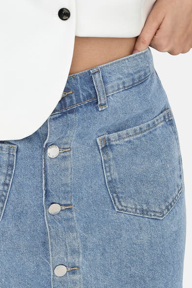 Jupe en jean bleu clair de ONLY avec boutonnage frontal et poches plaquées, portée avec un haut blanc.