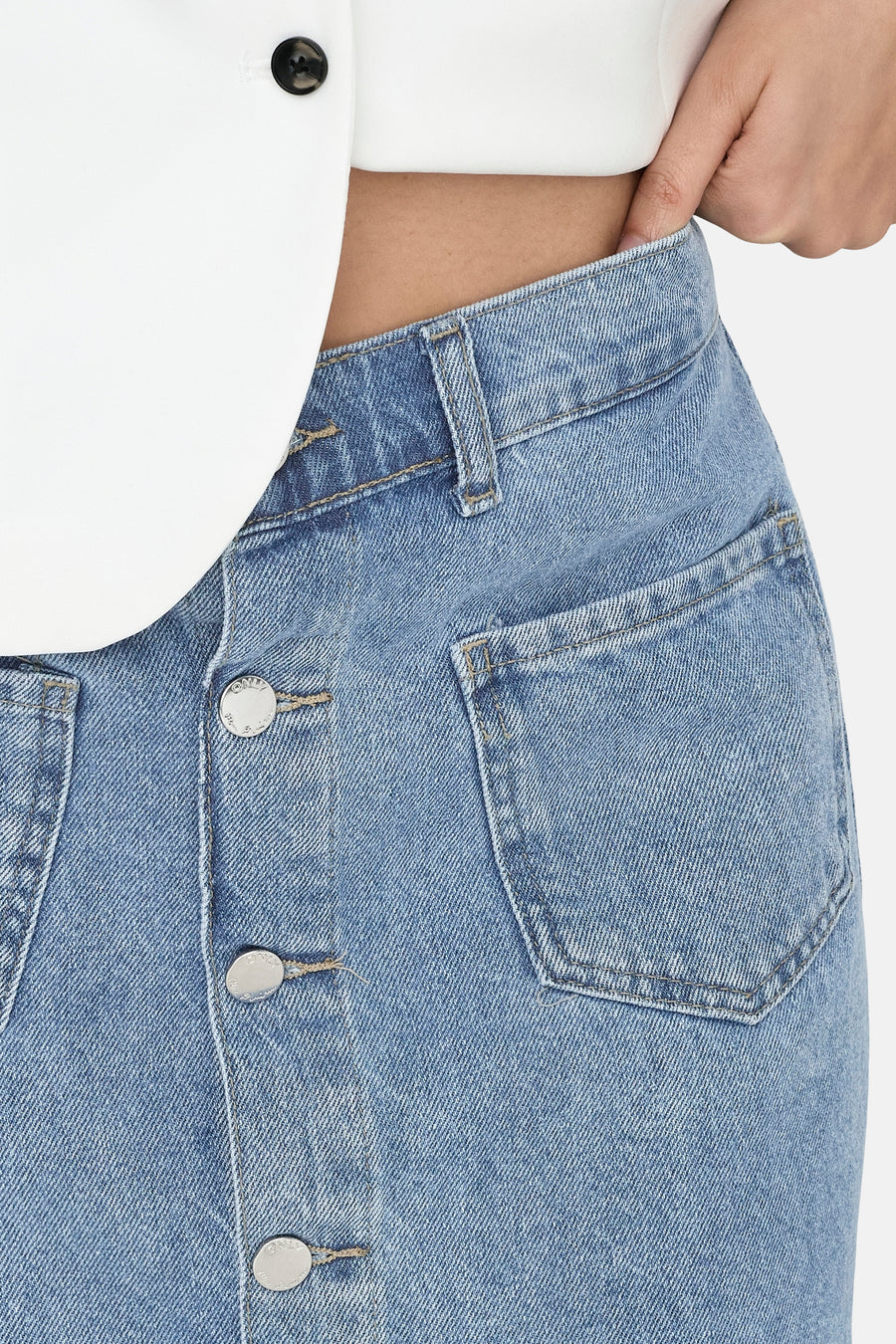 Jupe en jean bleu clair de ONLY avec boutonnage frontal et poches plaquées, portée avec un haut blanc.