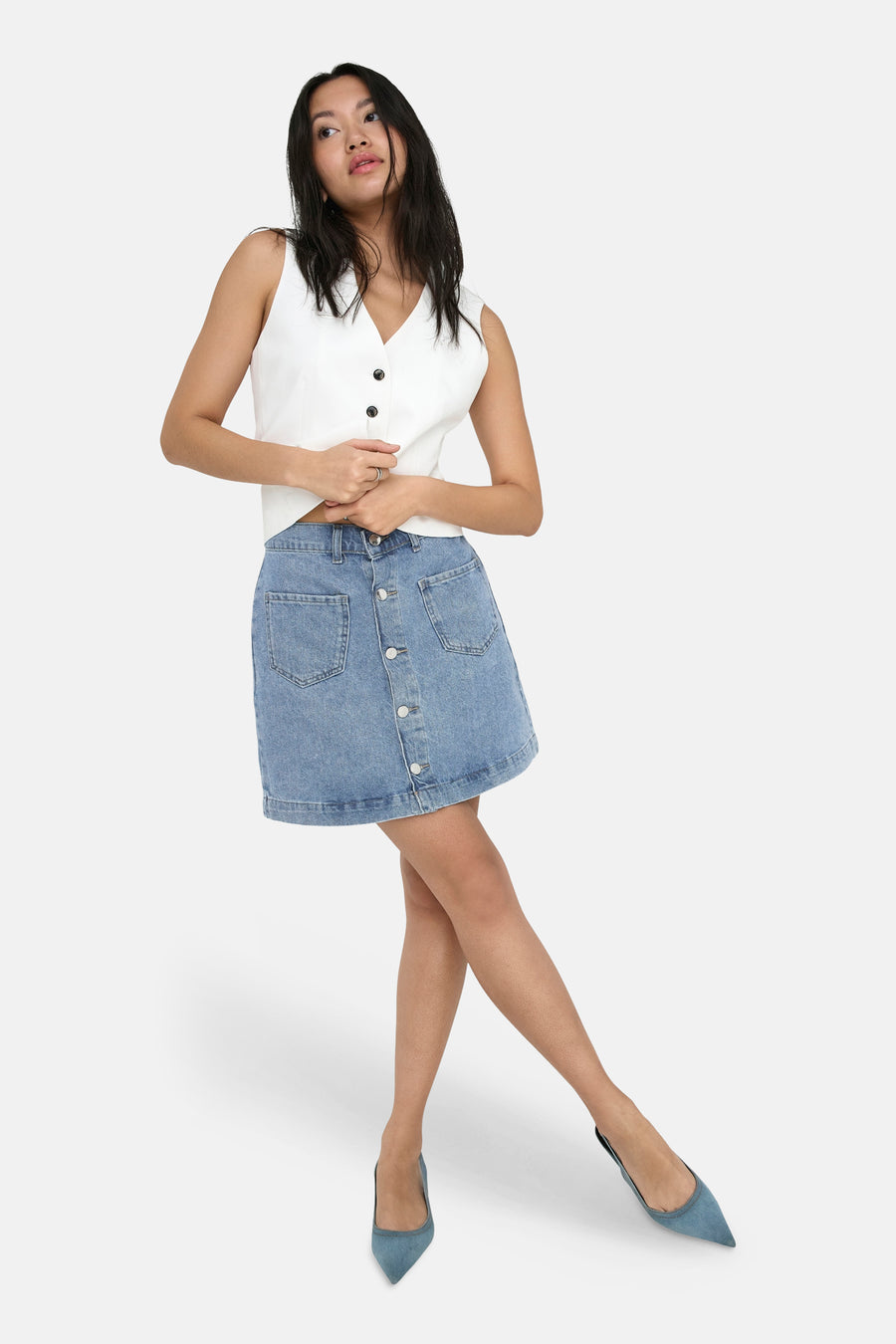 Jupe courte en denim bleu clair de ONLY®, boutonnée sur le devant avec poches plaquées, portée avec un haut blanc.