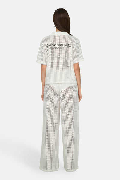 Chemisier à manches courtes en crochet blanc de ONLY, avec inscription au dos, porté avec un pantalon assorti.

