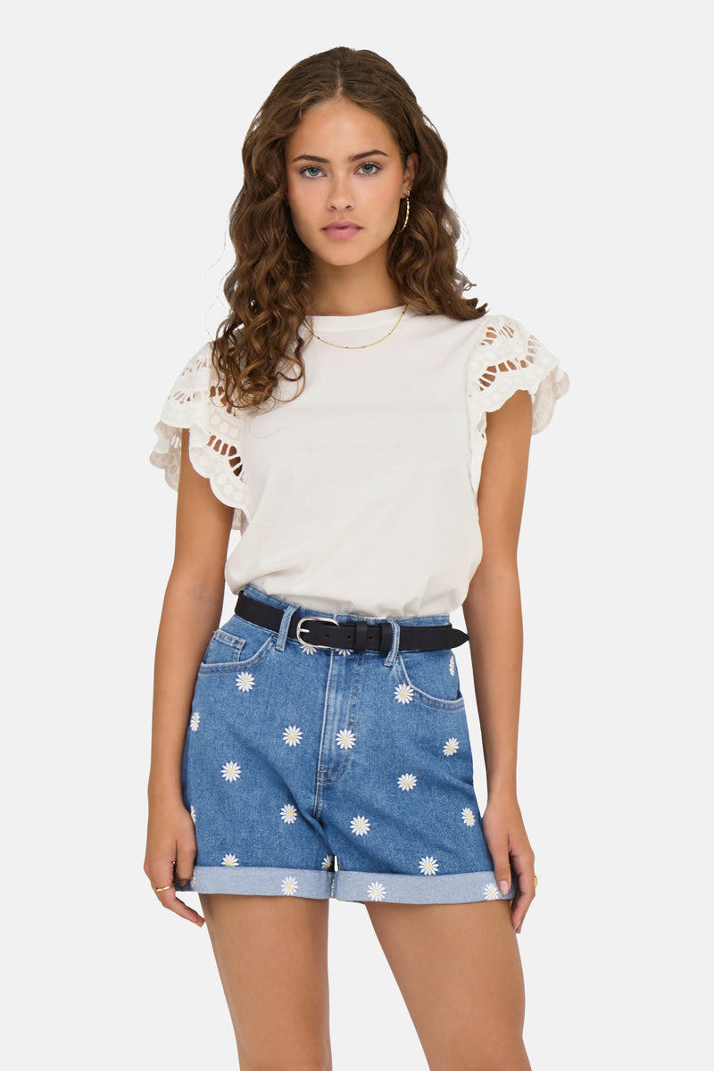 T-shirt blanc à manches courtes de ONLY, avec manches ajourées et porté avec un short à motif marguerites.

