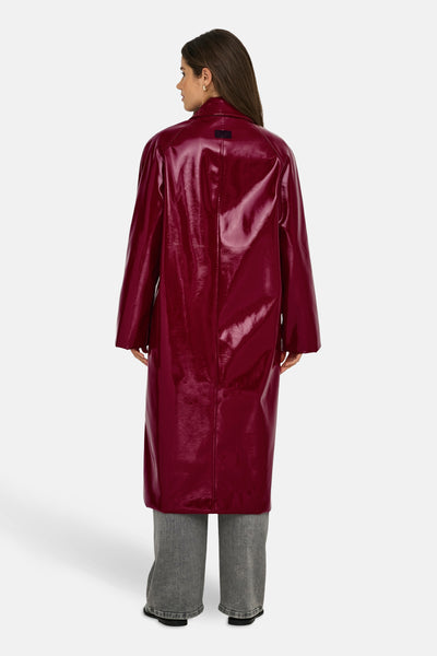Lange bordeaux fauxleren jas van ONLY, verticale naaddetail op de rug, gedragen met een grijze jeans.