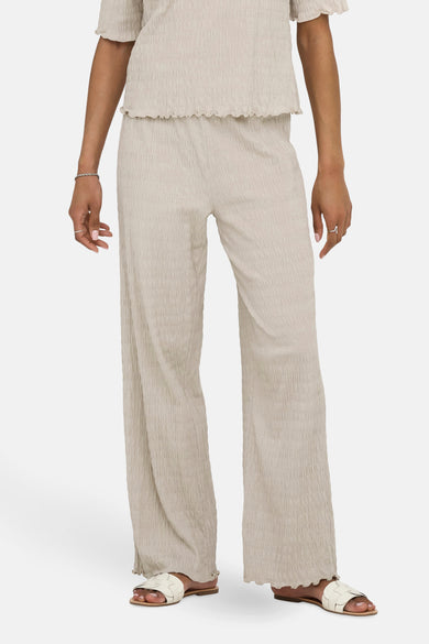 Beige texturiseerde broek van ONLY, met een wijde pasvorm en zichtbare witte sandalen.