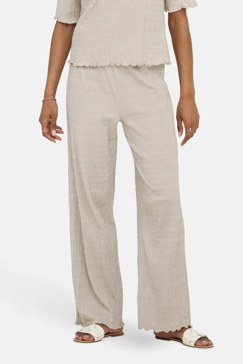 Beige texturiseerde broek van ONLY, met een wijde pasvorm en zichtbare witte sandalen.