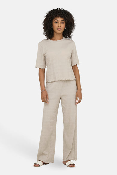 Beige broek van ONLY, met een geplooide textuur en een losse pasvorm, gedragen met witte sandalen.