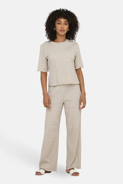 Beige broek van ONLY, met een geplooide textuur en een losse pasvorm, gedragen met witte sandalen.