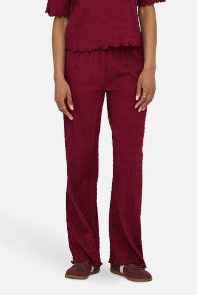 Gekreukte bordeauxrode broek van ONLY, gedragen met een bijpassend topje en bruine sneakers.