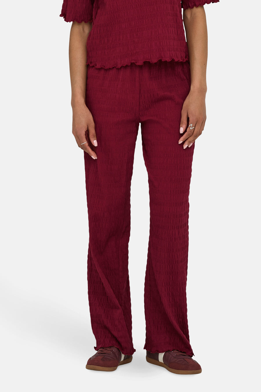 Gekreukte bordeauxrode broek van ONLY, gedragen met een bijpassend topje en bruine sneakers.