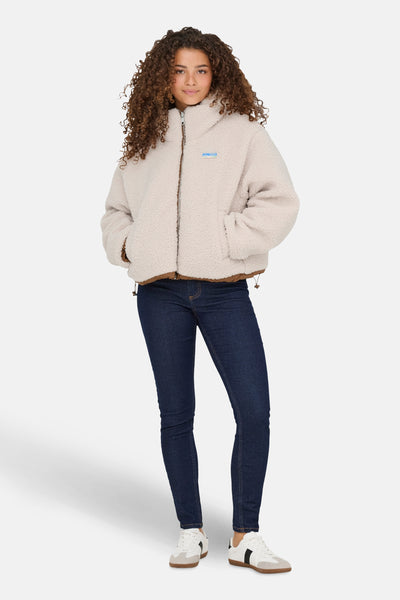 Veste courte écru de ONLY, avec doublure marron, portée avec un jean bleu foncé et des baskets blanches.

