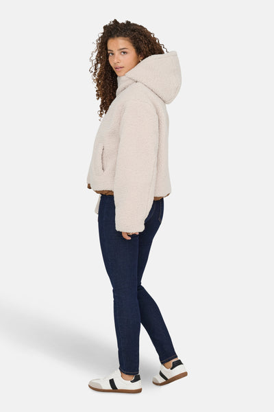 Veste courte écru de ONLY, avec capuche et finitions marron, portée avec un jean bleu marine et des baskets blanches.
