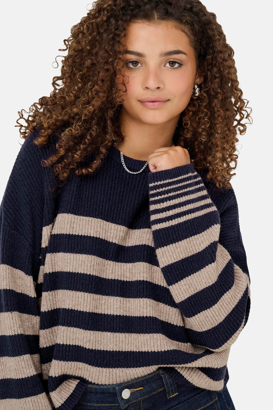Pull bleu à col rond de ONLY, avec motif rayé beige et porté avec un jean.
