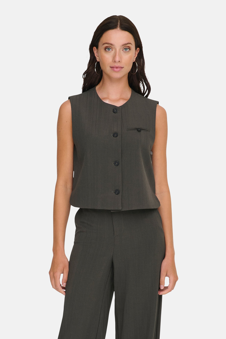 Gilet brun par ONLY, avec boutons décoratifs et une petite poche, porté avec un pantalon assorti.
