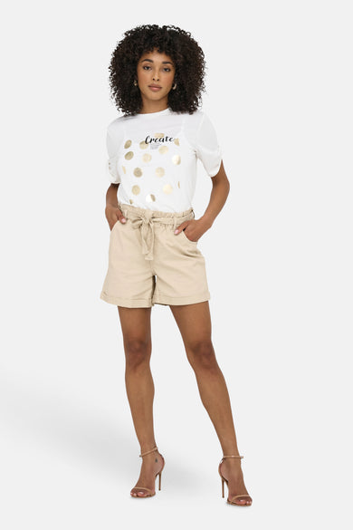 Korte beige short van JDY met een strikceintuur, gedragen met een bedrukt T-shirt en sandalen met hoge hakken.