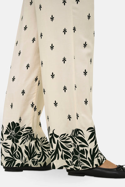 Pantalon écru de JDY, avec motif floral noir sur le bas et feuilles noires éparses.