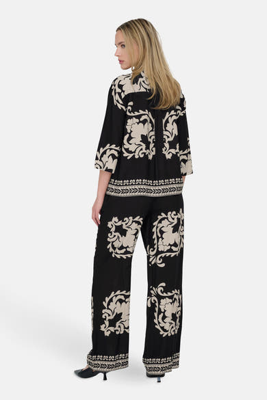 Chemise noire à manches longues de JDY avec un motif floral beige, portée avec un pantalon assorti.