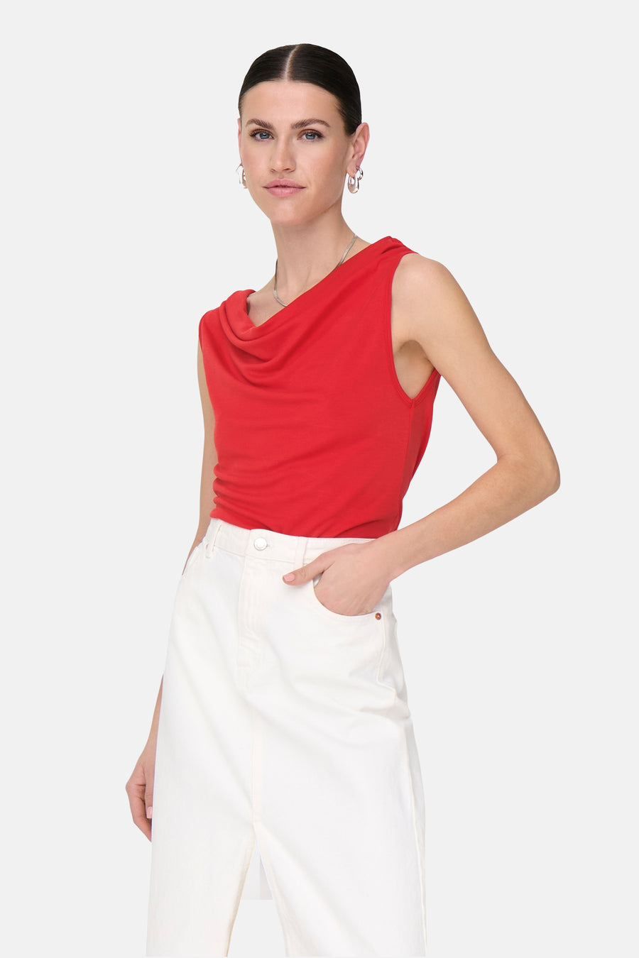 Top rouge sans manches de JDY, avec un col drapé et porté avec une jupe blanche.
